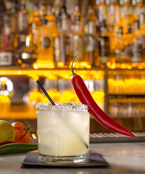 Cocktail with a pepper sitting on the lip of the glass.